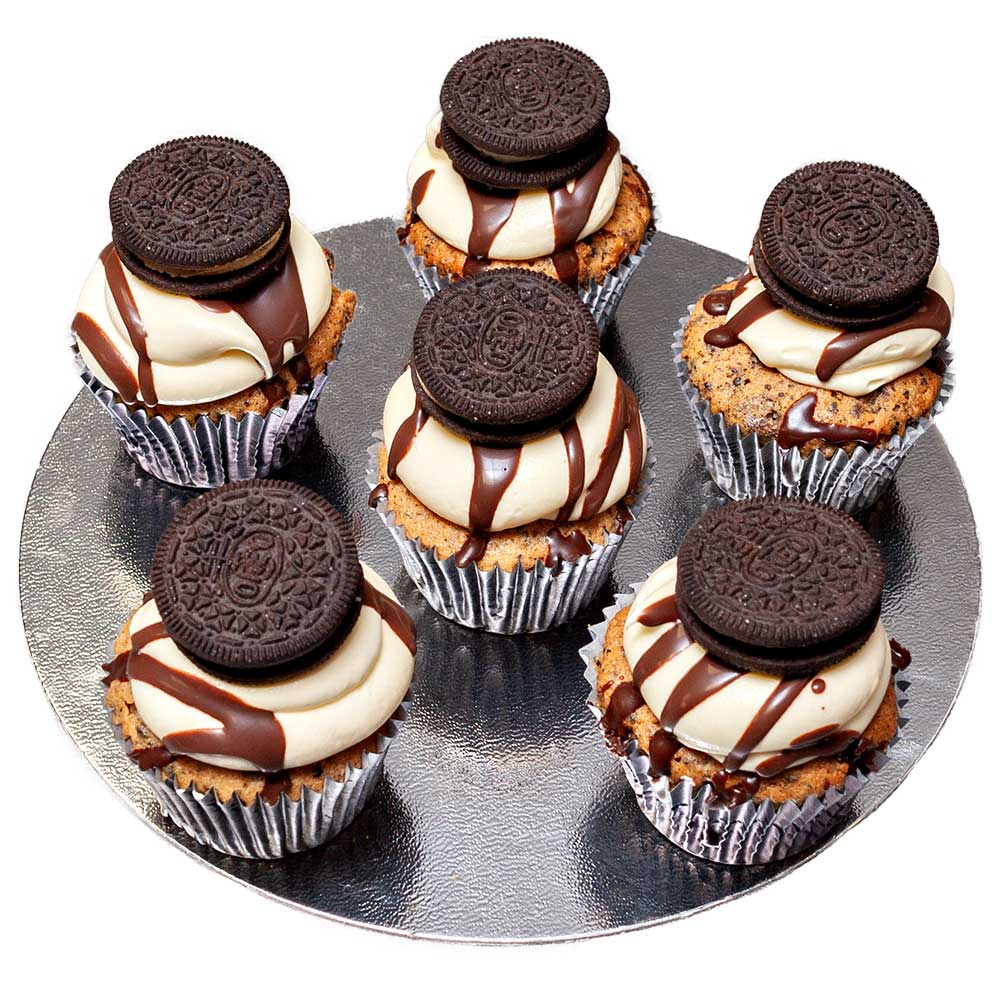 Six vanilla sponge cupcakes topped with butter cream drizzled with chocolate sauce and an Oreo biscuit.