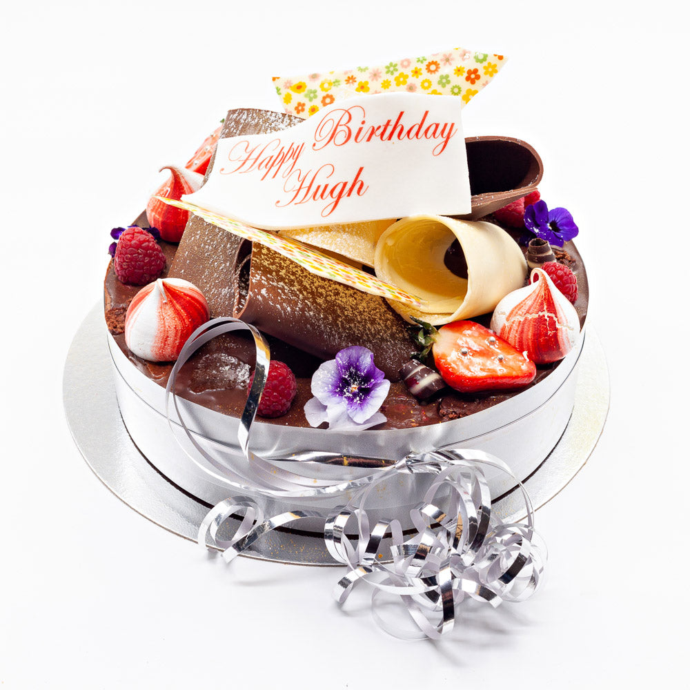 A luxury cake topped with lots of huge chocolate curls, meringue swirls, edible flowers, summer fruits and an edible inscription on top.