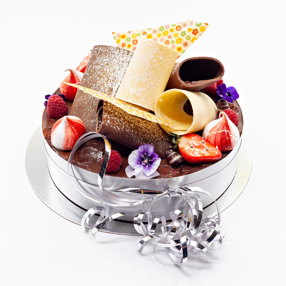A luxury cake topped with lots of huge chocolate curls, meringue swirls, edible flowers, summer fruits.
