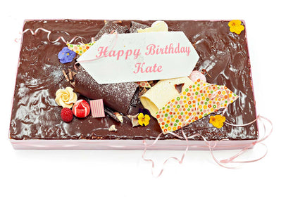 Rectangular birthday cake with a chocolate ganache on top and decorated with chocolate decorations and edible flowers.