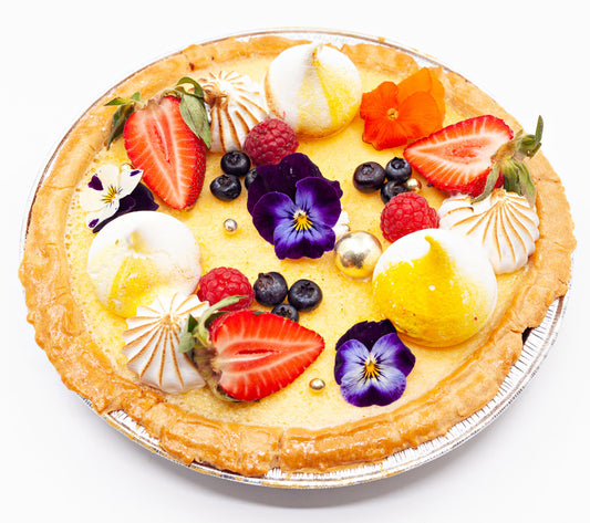 Deep-filled lemon meringue tart, topped with lemon swirls, edible flowers and summer fruits.