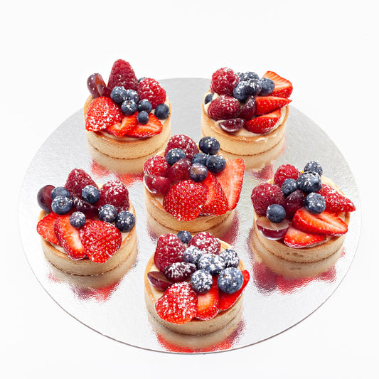 Six summer fruit tartlets, each topped with strawberries, blueberries, raspberries and grapes