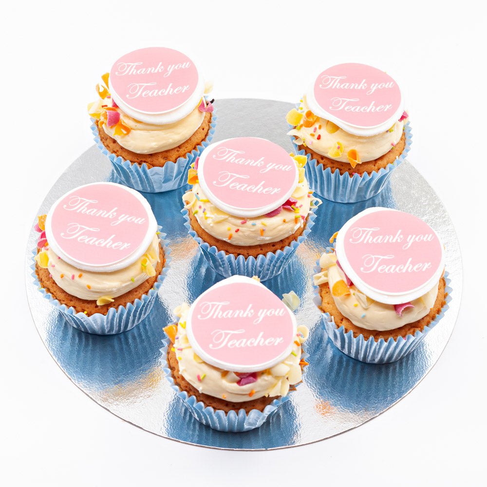 Six vanilla sponge cupcakes, each topped with butter cream and an edible disc that says 'Thank you, teacher" on it.