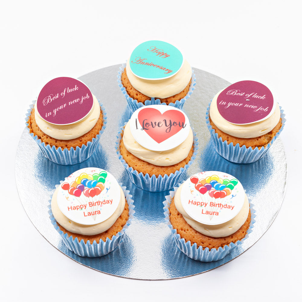 Six vanilla sponge cupcakes, each topped with butter cream and a colourful edible disc with an inscription on it