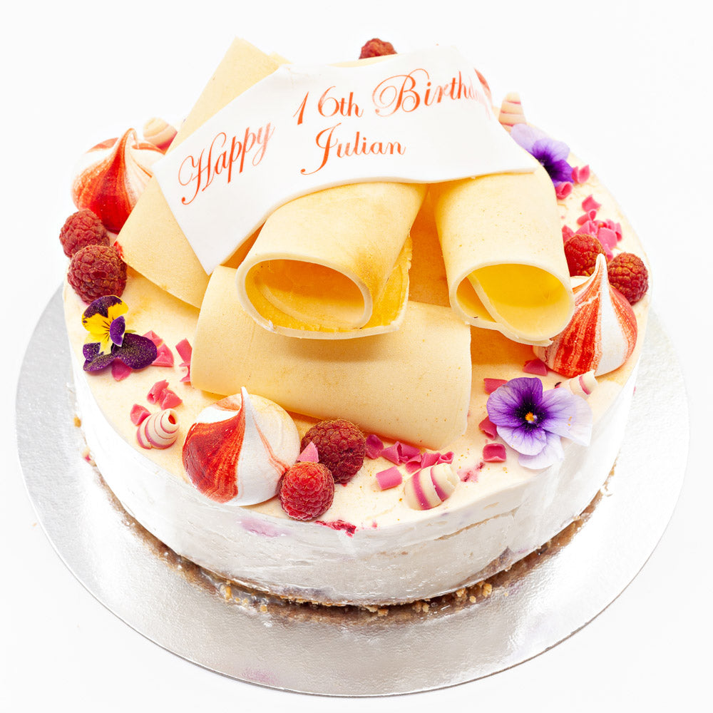 A white chocolate cheesecake topped with large white chocolate curls, summer fruits, meringue swirls and summer flowers